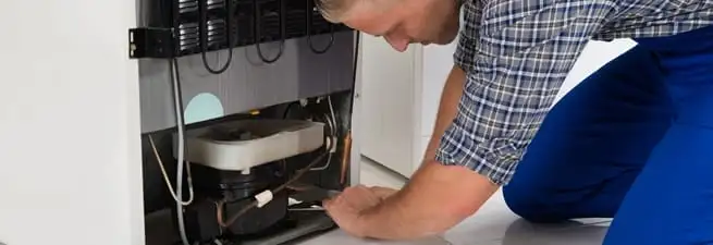 Refrigerator repair technician servicing the compressor and condenser area in Stockton, CA