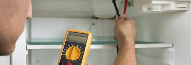 Refrigerator repair technician testing electrical components with a multimeter in Stockton, CA